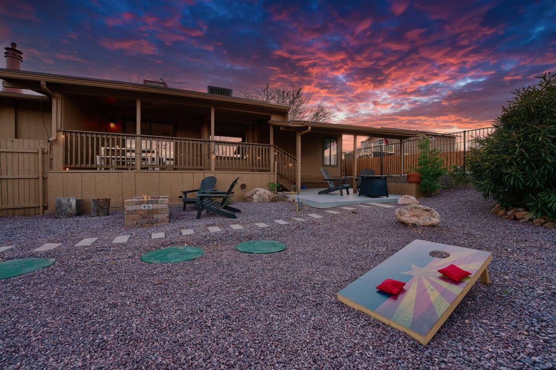 Backyard at sunset with a firepit, Adirondack chairs, and cornhole